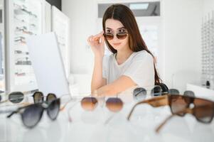 en ung kvinna väljer på solglasögon i ett optik Lagra foto