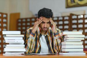 porträtt av glad manlig internationell indisk studerande med ryggsäck, inlärning Tillbehör stående nära bokhyllor på universitet bibliotek eller bok Lagra under ha sönder mellan lektioner. utbildning begrepp foto