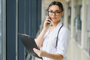 Lycklig läkare bär labb täcka talande på smart telefon på sjukhus foto