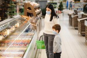 porträtt av en mor och henne liten son bär skyddande ansikte mask på en mataffär under de coronavirus epidemi eller influensa utbrott. tömma Plats för text foto