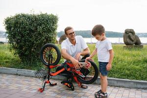 Lycklig far och hans son har roligt tillsammans på de grön parkera, fixering cykel tillsammans. fars dag foto