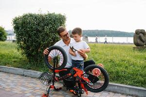 Lycklig far och hans son har roligt tillsammans på de grön parkera, fixering cykel tillsammans. fars dag. foto