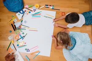 barn teckning på golv på papper. förskola pojke och flicka spela på golv med pedagogisk leksaker - block, tåg, järnväg, plan. leksaker för förskola och dagis. barn på Hem eller dagis. topp se. foto