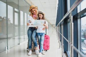 mor och liten dotter med bagage och Karta på flygplats terminal redo för semester. foto