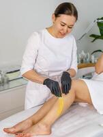kvinna kosmetolog utför sötning peeling på henne ben foto