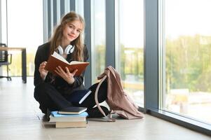 flicka leende. skön skol leende medan Sammanträde nära fönster och läsning bok foto