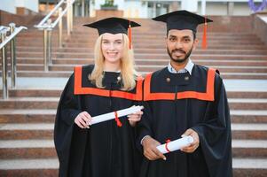 utbildning, gradering och människor begrepp - Lycklig internationell studenter i murbruk styrelser och ungkarl klänningar. foto