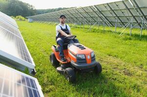 en man klipper de gräs nära de sol- paneler. grön energi foto