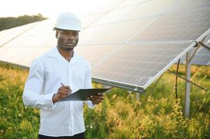 afrikansk amerikansk tekniker kontrollera underhållet av solpanelerna. svart man ingenjör på solstationen. foto