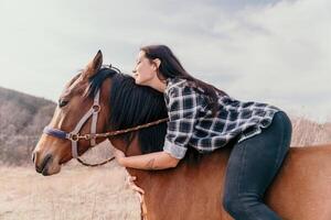 ung Lycklig kvinna i hatt med henne häst i kväll solnedgång ljus. utomhus- fotografi med mode modell flicka. livsstil humör. begrepp av utomhus- ridning, sporter och rekreation. foto