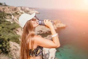kvinna resa hav. Lycklig turist dryck vatten på varm sommar dag. kvinna resande utseende på de kant av de klippa på de hav bukt av berg, delning resa äventyr resa foto