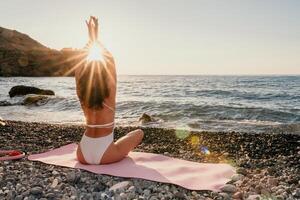 kvinna hav yoga. Lycklig kvinna i vit baddräkt och boho stil armband praktiserande utomhus på yoga matta förbi hav på solnedgång. kvinnor yoga kondition rutin. friska livsstil, harmoni och meditation foto