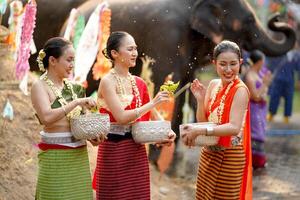 grupp av thai kvinnor gods thai traditionell klänning spela till stänk vatten på de thai ny år dag eller songkran festival i en roligt sätt på elefant och lugg av sand bakgrund. foto