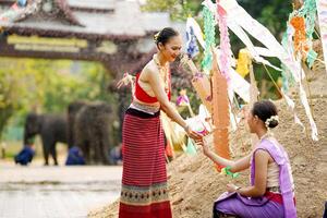 skön thai ung lady gods thai traditionell klänning ge en små papper flaggor till henne vänner till hjälp plats i de sand i tempel på de songkran festival. foto