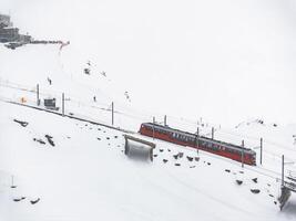 antenn se av röd tåg i snöig zermatt, schweiz med skidåkare i bakgrund foto