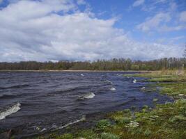 stark vind höjer en Vinka med vit skum, vår landskap förbi de sjö foto