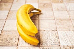 två mogen gul bananer i en ringa på en rutig trä- yta foto