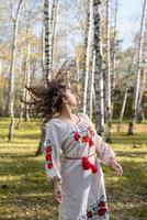 vacker kvinna i ukrainska nationella traditionella kostymkläder dansar i skogen foto