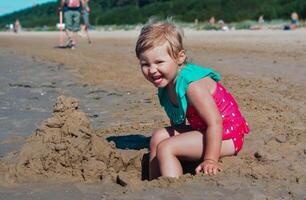 ung Lycklig barn flicka av europeisk utseende ålder av 4 har roligt på de strand och byggnad sand slott, skrattar och ser på de kamera, tropiskt sommar yrken, helgdagar.a barn åtnjuter de sea.copy Plats foto