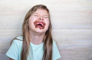 Lycklig och skrattande liten flicka äter choklad smutsig ansikte. stänga upp av unge med smutsig ansikte i choklad . foto