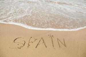 Spanien text på de strand med Vinka och klar blå hav. brev Spanien på de hav Strand, meddelande handskriven i de gyllene sand på skön strand bakgrund. högtider i Spanien begrepp. hög kvalitet Foto