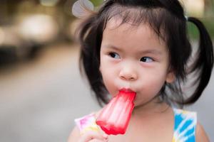 huvudskott bedårande asiatisk liten flicka äter röd glass. barn på 3 år. på sommaren eller våren. foto