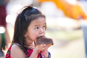 ett sött barn äter choklad. bedårande unge flicka njuta av att äta med picknick mellanmål i en sommarsemester. bebis i åldern 4-5 år. foto