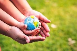 miljövänligt koncept. händerna på barn och vuxna håller världen säker från den globala uppvärmningen. ta hand om vår värld. världs miljö dagen. foto