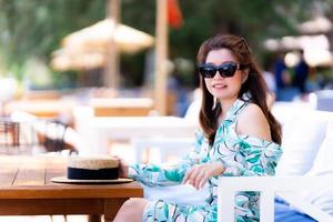 vackra kvinnor ler snygga bär blommig grön klänning och solglasögon. porträtt mode vacker kvinna sitter på café restaurang. foto