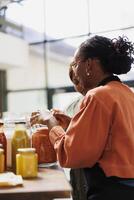 afrikansk amerikan Säljare i en Lagra, erbjudanden råd och serverar henne kunder med nyligen skördade, organisk bio mat. sida se av henne samspel med ett person i eco vänlig lokal- mataffär. foto