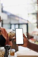 detaljerad se av cell telefon grep förbi afrikansk amerikan person, visning isolerat vit skärm för hållbar bio mat Lagra reklam. närbild av mobil enhet som visar tom attrapp mall. foto