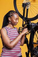 engagerad svart kvinna i närbild skott använder sig av expert- verktyg till reparera och fixera cykel vev ärm. detaljerad se av sportig afrikansk amerikan kvinna lagning skadad cykel förbi använda professionell multiverktyg. foto