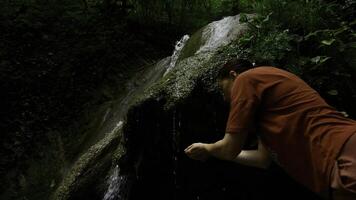 ung kvinna dricka vatten från kaskad vattenfall på djup tropisk regn skog. kreativ. kvinna vandrare dricka vatten från bergig vår. foto