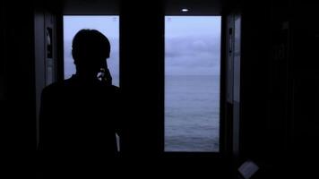 ung man stående Nästa till en tåg fönster och ser utanför stock klämma. man med smartphone ser genom de fönster på hav. foto