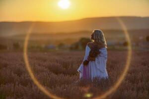 blond kvinna poser i lavendel- fält på solnedgång. Lycklig kvinna i vit klänning innehar lavendel- bukett. aromaterapi begrepp, lavendel- olja, Foto session i lavendel-