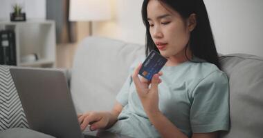 selektiv fokus, ung asiatisk kvinna Sammanträde på soffa innehav kreditera kort framställning uppkopplad betalning för inköp i webb Lagra använder sig av bärbar dator foto