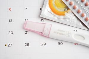 graviditet testa med födelse kontrollera piller och kondom för kvinna på kalender, ägglossning dag. foto