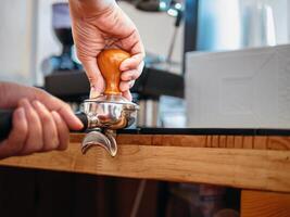 hand av en Barista innehav en portafilter och en kaffe manipulera framställning ett espresso kaffe. Barista trycker på jord kaffe använder sig av en manipulera i en kaffe affär foto