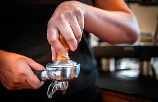 hand av en Barista innehav en portafilter och en kaffe manipulera framställning ett espresso kaffe. Barista trycker på jord kaffe använder sig av en manipulera i en kaffe affär foto