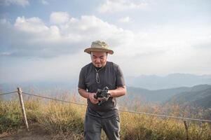 asiatisk fett man innehav kamera stativ med skön se av khao san nok wua berg kanchanaburi.khao san nok wua är de högsta berg i khao laem nationell parkera. den är 1767 meter ovan hav nivå foto