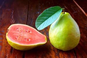 närbild guava frukt, rosa, färsk, organisk, med löv, hela och skivad, på rustik trä- tabell foto