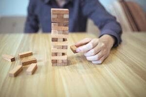 företag strategi begrepp med händer spelar en trä- blockera torn spel, symboliserar risk och stabilitet. planera risk förvaltning foto