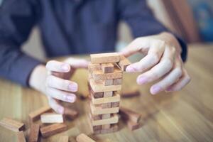 företag strategi begrepp med händer spelar en trä- blockera torn spel, symboliserar risk och stabilitet. planera risk förvaltning foto