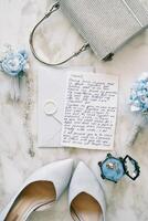 bröllop svära lögner på ett kuvert Nästa till de brud skor och handväska på en marmor tabell foto