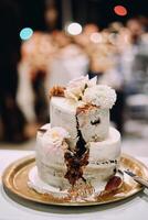två skikt bröllop kaka dekorerad med blommor med en skära ut sektor står på en bricka på de tabell foto