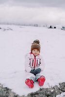liten flicka Sammanträde på en snöig bete foto