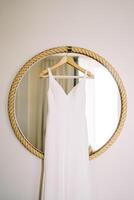 bröllop klänning hänger på en galge på en runda spegel i en rep ram på de vägg i de rum foto
