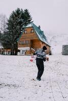 mamma snurrar en liten flicka i henne vapen på en snöig kulle nära de hus foto