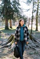 ung lady med en ryggsäck i henne hand promenader genom en barr- skog och utseende bort foto