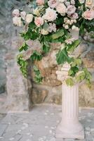 frodig bukett av blommor står i en vas på en piedestal nära en sten vägg i de trädgård foto